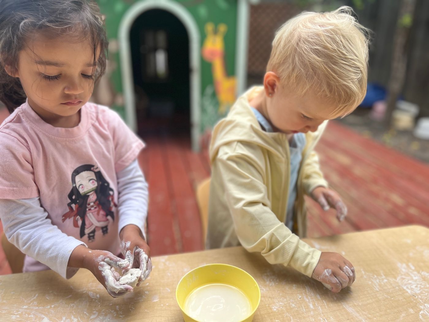 Children kneading dough together at an outdoor table